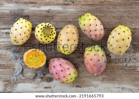 Several ripe prickly pears lie on a board of old weathered wood. A fruit is cut open.