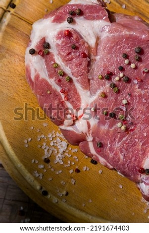 Raw beef meat with salt and peppercorns on a wooden board and wooden table. Vertical orientation