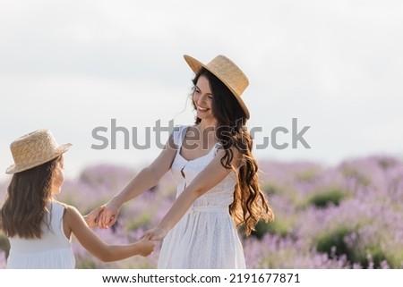 brunette woman with long hair holding hands with daughter in countryside