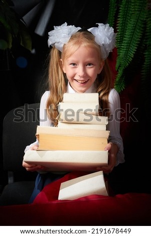Girl who is elementary school children in uniform having photo shoot in school holiday on September 1 on black background with books. Holiday of the beginning of school and studing in Russia