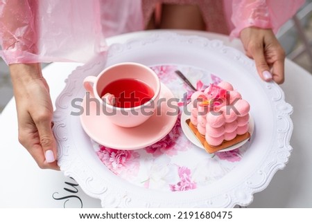 Sugar pink neo cube ball velours mousse cake dessert on plate on table near cup of tea in cropped woman hands with manicure. Cafe or bakery. Dessert table birthday festive event party. High angle
