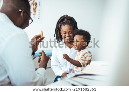 Smiling male pediatrician in white medical uniform holding clipboard, listening to young mother with kid son at checkup meeting, professional children doctor consultation, healthcare concept.