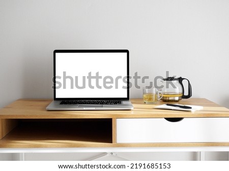Laptop computer with white blank screen mock up. Workspace in minimalist scandinavian interior with wooden furniture and cup of green tea.                               