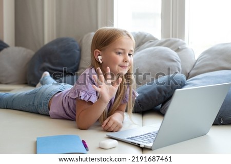 A cute girl looks at a laptop screen, makes gestures, showing sign language, takes part in online classes, communicates with a teacher using a video conference application with a speech therapist
