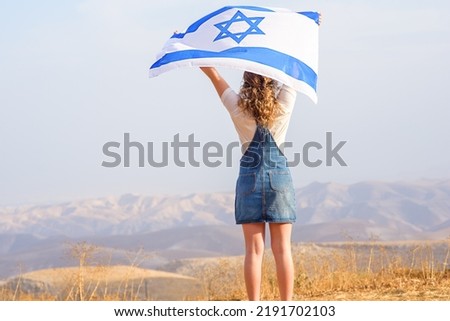 Teen curly hair Jewish girl standing with the flag of Israel on the amazing valley and blue sky background. Memorial day-Yom Hazikaron,Patriotic holiday Independence day Israel Yom Ha'atzmaut Royalty-Free Stock Photo #2191702103