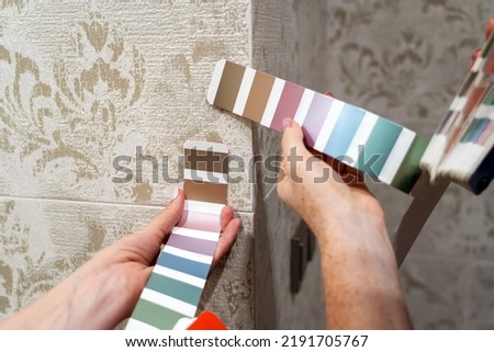 Two women choosing samples of furniture paint. Interior designer consulting client looking at color swatch. Couple with palette of colors selects harmonious color of furniture with existing tiles 