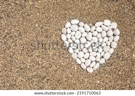 White smooth pebble romantic heart shape on sunny sand beach top view. Abstract romance serene spa valentine symbol summer travel vacation nature destination harmony life balance peaceful and love