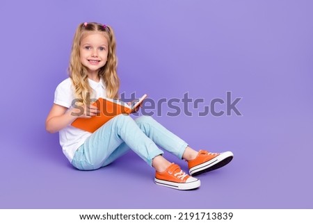 Full length photo of cheerful little girl tails sit read book do homework dressed stylish white blouse isolated on violet color background Royalty-Free Stock Photo #2191713839