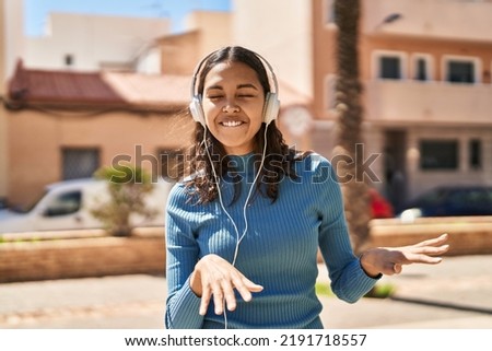 Young african american woman listening to music and dancing at street