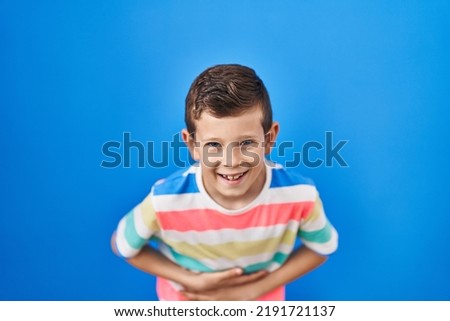 Young caucasian kid standing over blue background smiling and laughing hard out loud because funny crazy joke with hands on body. 