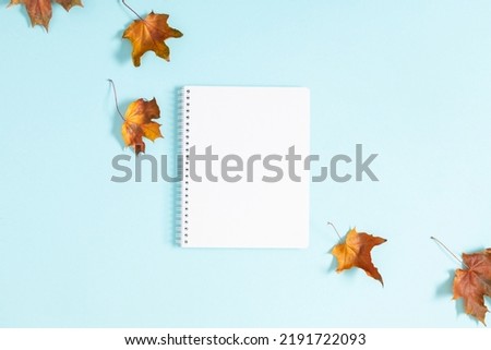 Autumn creative composition with leaves and notebook. Empty notepad mockup, dried leaves on pastel blue background. Fall concept. Autumn background. Flat lay, top view, copy space
