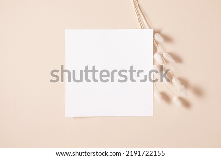 White paper empty blank, dry flowers, dried branch on beige background. Invitation card mockup on beige table. Flat lay, top view, copy space, mockup