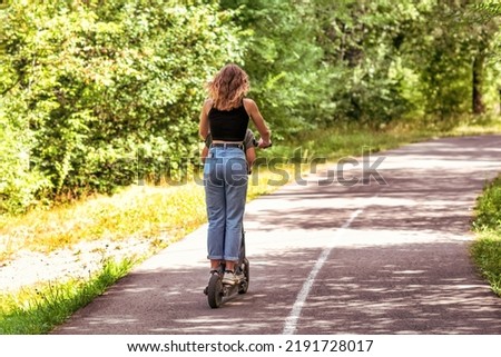 A young woman is riding on the electric scooter in a summer park. Royalty-Free Stock Photo #2191728017