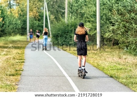A young woman is riding on the electric scooter in a summer park. Royalty-Free Stock Photo #2191728019