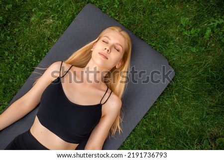 The girl lies with her eyes closed, on a yoga mat, rest after training, appeasement, meditation, karemat on the background of grass, outdoor sports, exercises, top view, copy space Royalty-Free Stock Photo #2191736793