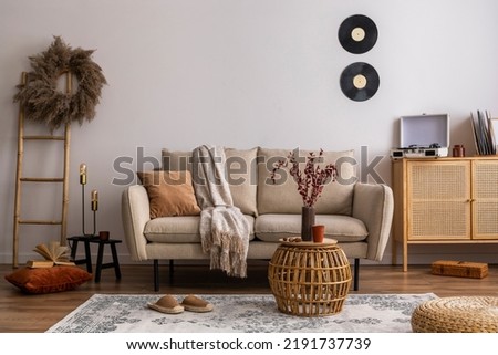 Interior design of harmonized living room with design beige sofa carpet, pillow, plaid, coffee table, vinyl recorder and elegant personal accessories. Beige wall. Minimalist home decor. Template.	
