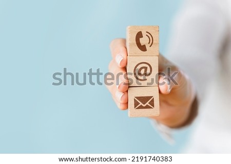 Female hand holding wooden block cube symbol telephone, envelope email and address sign. Website page contact us or social media concept
