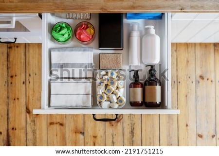 top view of opened drawer with towels, washing sponge, detergent bottles and dishwashing tablets in plastic box in modern kitchen cabinet in apartment, storage concept Royalty-Free Stock Photo #2191751215