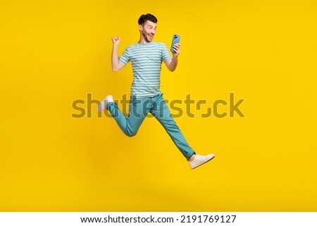 Full size body photo of young funny guy jump air run take his prize bet online money phone isolated on yellow color background