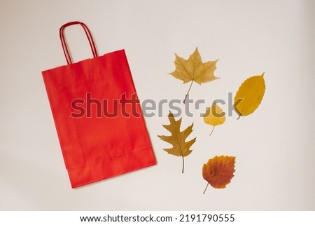 Autumn flat lay. A craft red bag and autumn fallen leaves side by side on a light background. Autumn concept of discounts and sales