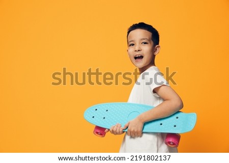 a little preschool-age boy stands on an orange background in a white T-shirt, holding a skate in his hands, standing sideways to the camera and shouting merrily