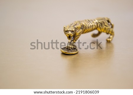 A bronze figure of a tiger with a coin - the symbol of financial well-being and wealth  on a golden background, Copy space