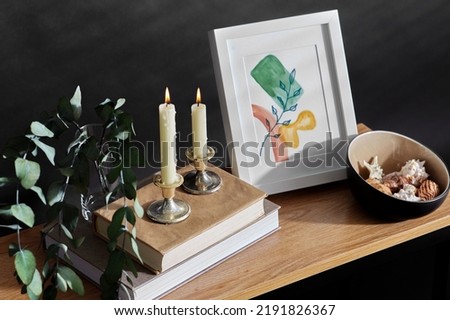 interior and home decor concept - close up of bench with burning candles, picture in frame, books, seashells and eucalyptus branches over black background