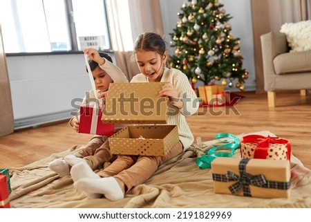 christmas, winter holidays and childhood concept - happy little girl and boy opening gifts sitting on floor at home