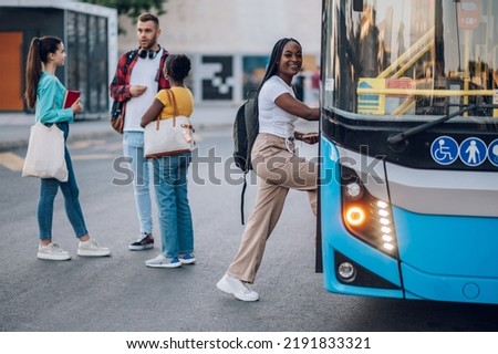 Diverse group of friends waiting for a bus while at a bus stop. Riding, sightseeing, traveling to work, city tour, togetherness. Focus on a beautiful african american woman entering the bus.