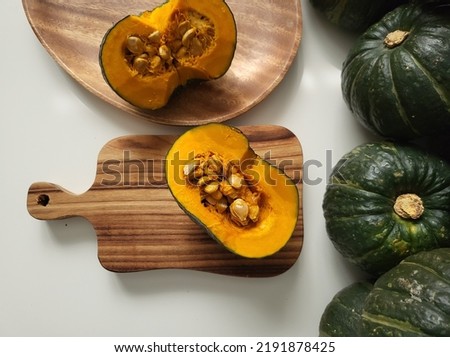 Wooden chopping board and wooden plate on a white table. Pumpkin and pumpkin seeds cut in half.
