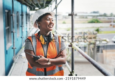 A happy, smiling and cheerful young black woman or senior construction industry worker standing at a building site. A professional female employee working at housing or property development location Royalty-Free Stock Photo #2191879449