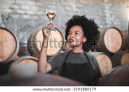 Black woman tasting wine at a winery, looking and checking the color and quality of the years produce. Young African American sommelier proud of the new addition, analyzing white wine in a cellar Royalty-Free Stock Photo #2191880179