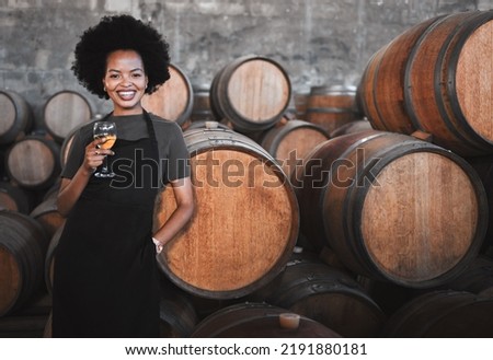 Portrait of a young woman winemaker standing with a glass with wooden barrel of red wine in a winery cellar or distillery. Entrepreneur or business owner working for startup success business success Royalty-Free Stock Photo #2191880181