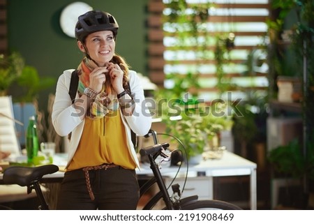 smiling trendy middle aged business woman in bike helmet with bike in modern eco office.
