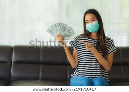 Portrait beautiful young asian woman with mask on sofa show money or cash at home Royalty-Free Stock Photo #2191910417