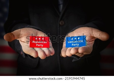 Democrats vs republicans. the concept of choosing a political party or ideology. A male politician offers to make a choice against the background of the American flag. Royalty-Free Stock Photo #2191944745
