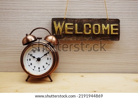 Welcome Sign with alarm clock on wooden background