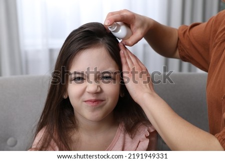 Mother using lice treatment spray on her daughter's hair indoors