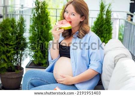 young pregnant woman eating watermelon on the balcony at home