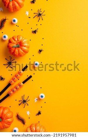 Halloween party concept. Top view vertical photo of cocktail straws pumpkins spiders centipedes creepy eyeballs and confetti on isolated orange background