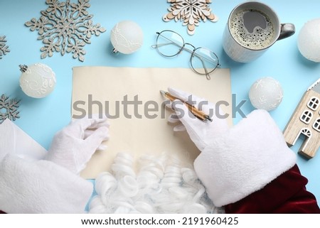 Top view of Santa writing letter at light blue table, closeup. Space for text
