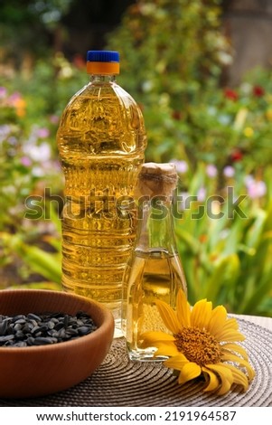 Bottles of sunflower oil and seeds in bowl on table outdoors