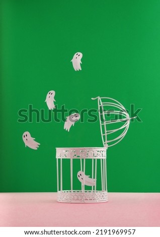 Halloween concept with bird cage and ghosts on pastel pink and green background. Scary and spooky concept. Modern aesthetic.