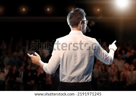 Motivational speaker with headset performing on stage, back view