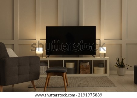 Modern TV on cabinet, armchair and lamps indoors. Interior design Royalty-Free Stock Photo #2191975889