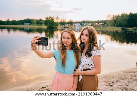 Vacation, relax, active lifestyle concept. Two teenager girls friends having fun, laughing, taking selfie by smartphone at nature by the lake.