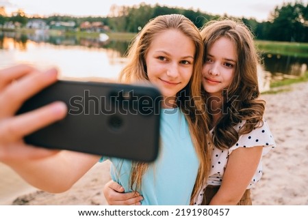 Vacation, relax, active lifestyle concept. Two teenager girls friends having fun, laughing, taking selfie by smartphone at nature by the lake.