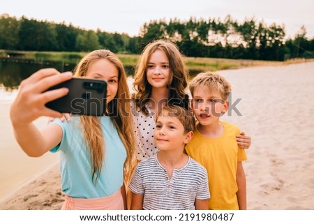 Vacation, relax, active lifestyle concept. Family four brothers and sisters in bright colorful clothes having fun, laughing, taking selfie by smartphone at nature by the lake.