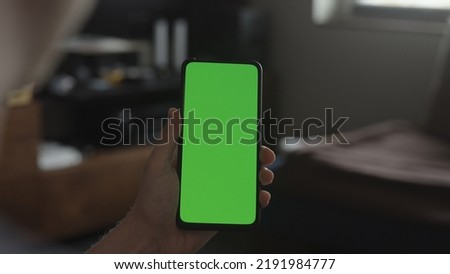 Man show and use phone with green screen indoor in living room
