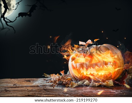 Halloween pumpkin with fire flames on wooden planks. Shinning moon on background